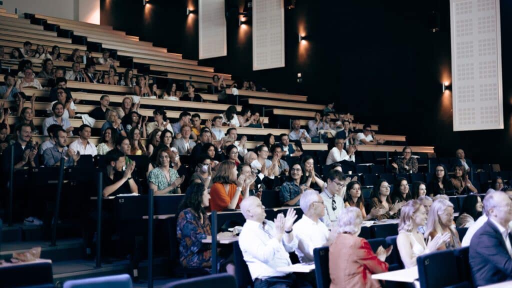 Public vu de face, applaudissant dans un amphithéâtre.